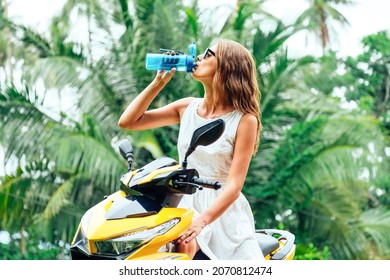 Portrait of young woman on scooter drinking water from reusable bottle - Shutterstock ID 2070812474