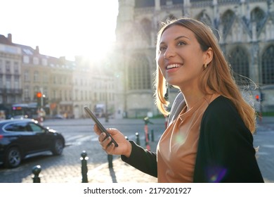 Portrait of young woman on side of road waiting a taxi cab holding a smart phone. Calling a taxi with a phone app concept.