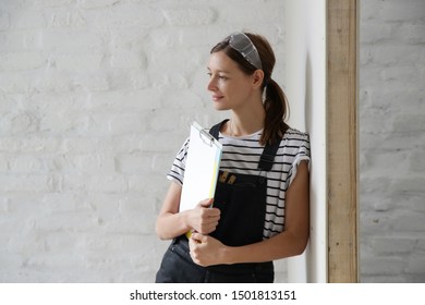 Portrait Of A Young Woman In Overalls And Protective Working Glasses Taking A Break In The Middle Of DIY Home Improvement Project