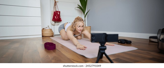 Portrait of young woman personal yoga instructor, recording workout video at home, using digital camera to vlog her exercises, using rubber mat. - Powered by Shutterstock