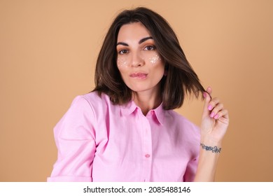 Portrait of a young woman in a pink dress on a beige background with shine glitter makeup and cute earrings posing positively, gentle romantic
