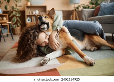 Portrait of young woman playing with happy dog fooling around on floor at home, copy space - Powered by Shutterstock