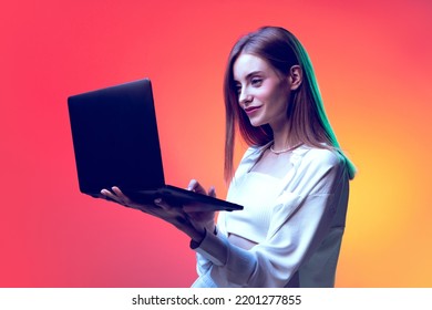 Portrait of young woman posing, having video conference on laptop isolated over red background in neon light. Online working. Concept of beauty, lifestyle, youth, emotions, facial expression, ad. - Powered by Shutterstock