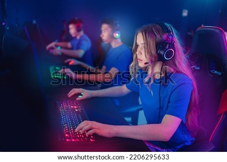 Portrait young woman pro gamer with headphones playing in online video game in net cafe, neon color light, soft focus. Cybersport team concept.