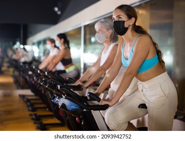 Portrait Of Young Woman In Protective Face Mask Training On Stationary Bike Workout In Gym