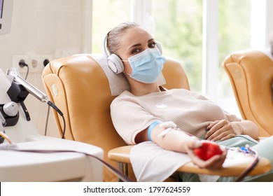 Portrait of young woman in protective mask looking at camera while lying on the couch and receiving a blood transfusion at hospital
