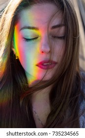 Portrait Of A Young Woman With A Rainbow Glare On Her Face. The Wind Blows Her Hair. Her Eyes Are Closed.