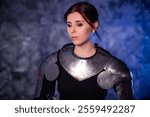 Portrait of a young woman with scars on her face, dressed in black clothes with steel knightly hands and a gorget, posing against an abstract background. Medieval fantasy girl.