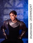 Portrait of a young woman with scars on her face, dressed in black clothes with steel knightly hands and a gorget, posing against an abstract background. Medieval fantasy girl.