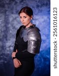 Portrait of a young woman with scars on her face, dressed in black clothes with steel knightly hands and a gorget, posing against an abstract background. Medieval fantasy girl.