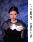 Portrait of a young woman with scars on her face, dressed in black clothes with steel knightly hands and a gorget, posing against an abstract background. Medieval fantasy girl.