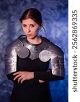 Portrait of a young woman with scars on her face, dressed in black clothes with steel knightly hands and a gorget, posing against an abstract background. Medieval fantasy girl.