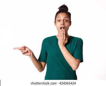 Portrait of young woman with shocked expression pointing away at copy space over white background