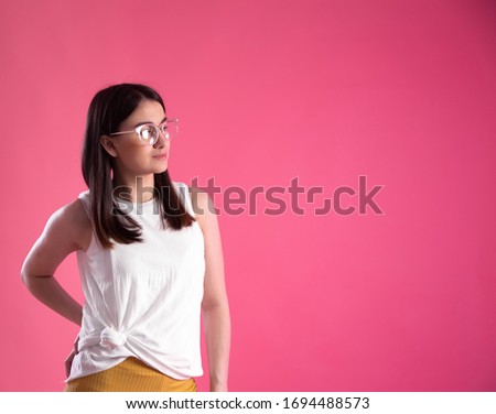 Portrait of a young woman showing emotions, wearing glasses on a pink isolated background.
