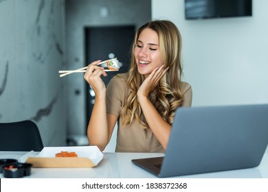 Portrait of a young woman sitting in front of a laptop computer eating a sushi