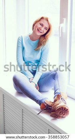 Portrait of young woman sitting and laughing on a windowsill
