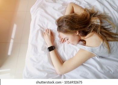 Portrait Of Young Woman With Smartwatches On Hand Sleep In White Bed. Concept Of Monitor Sleeping Patterns On Electronic Watch, Health Check Habbits