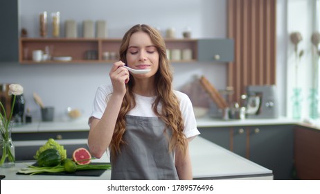 Portrait Of Young Woman Smelling Food At Home Kitchen. Pretty Housewife Tasting Fresh Meal At Home. Cheerful Female Chef Enjoying Food Taste Indoors. Joyful Woman Face At Modern Kitchen.