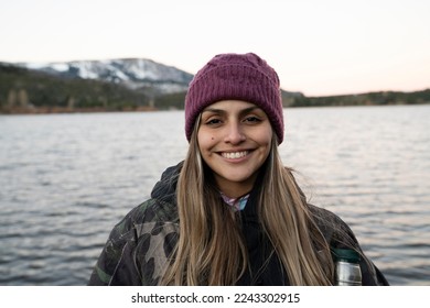 Portrait of a young woman smiling. The placid lake and mountain range in the background. Beautiful sunset colors in the environment.