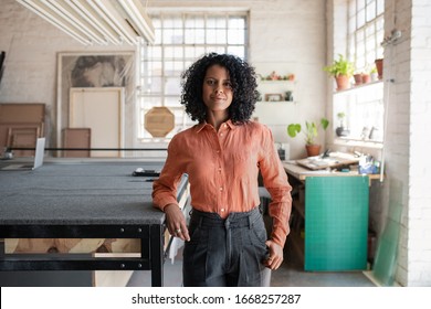 Portrait of a young woman smiling while standing next to a workbench in her picture framing studio - Powered by Shutterstock