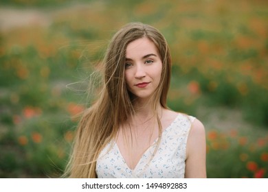 Portrait of young ?ute woman standing on poppy field dressed in white dress. Close up portrait of blonde woman on background of field. Relax and romance in one photo