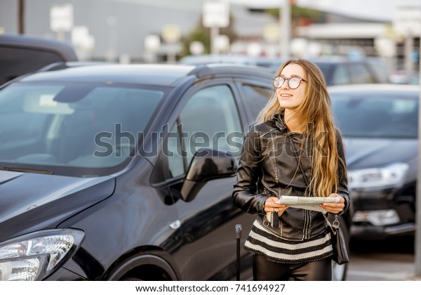 Portrait of a young woman\
standing with rental contract outdoors on the car parking near the\
airport