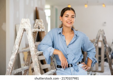 Portrait of young woman standing at stepladder in apartment during repair works.