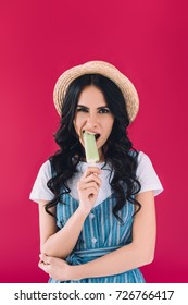 Portrait Of Young Woman In Straw Hat Eating Popsicle Isolated On Pink