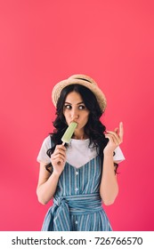 Portrait Of Young Woman In Straw Hat Eating Popsicle Isolated On Pink