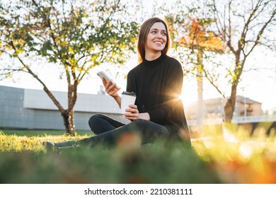 Portrait of young woman student with long hair using mobile phone in city park in golden hour