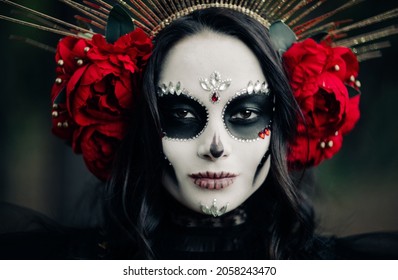 Portrait Of Young Woman With Sugar Skull Makeup And Red Roses Dressed In Black Costume Of Death As Santa Muerte. Day Of The Dead Or Halloween Concept.