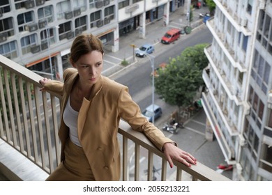 Portrait Of Young Woman In Suit Standing On Balcony With Busy City Street In Background	