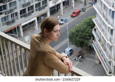 Portrait Of Young Woman In Suit Standing On Balcony With Busy City Street In Background	
