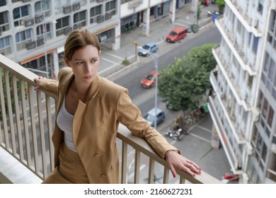 Portrait Of Young Woman In Suit Standing On Balcony With Busy City Street In Background	
