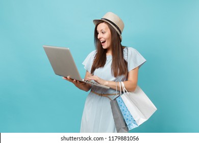 Portrait Of Young Woman In Summer Dress, Straw Hat Holding Packages Bags With Purchases After Online Shopping, Using Laptop Pc Computer Isolated On Blue Pastel Background. Copy Space Advertisement