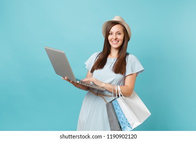 Portrait Of Young Woman In Summer Dress, Straw Hat Holding Packages Bags With Purchases After Online Shopping, Using Laptop Pc Computer Isolated On Blue Pastel Background. Copy Space Advertisement