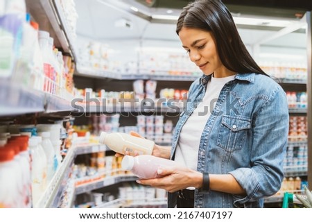 Portrait young woman in supermarket holding two bottles of yogurt reads labels compares chooses healthy dairy food Stockfoto © 