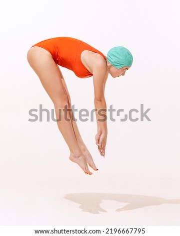 Portrait of young woman in swimming suit and cap jumping, diving into water isolated over grey studio background. Concept of beauty, fashion, vintage style, summertime, party. Copy space for ad