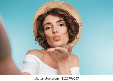 Portrait of a young woman taking a selfie and sending kiss isolated over blue background - Powered by Shutterstock