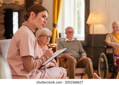 Portrait of young woman talking to group of senior people during therapy session at retirement home, copy space