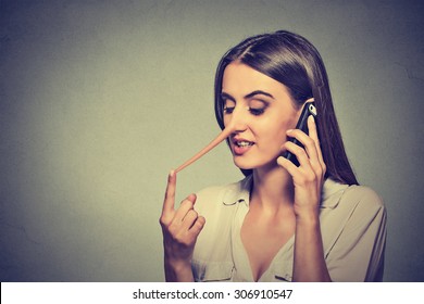 Portrait young woman talking on mobile phone telling lies has a long nose isolated on gray wall background 