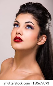 portrait of a young woman with tanned skin, blue contact lenses and red lipstick wearing long brown hair loose over studio background