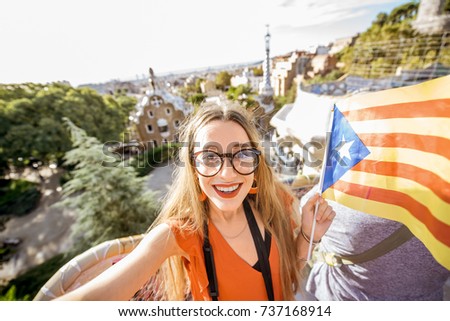 Portrait of a young woman tourist in red dress with catalan flag visiting famous Guell park in Barcelona