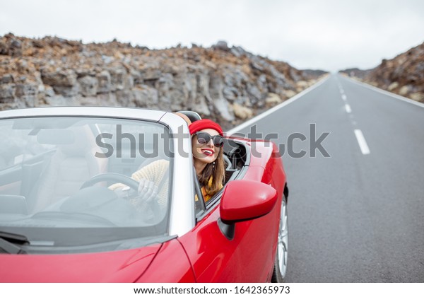 Portrait of a young woman traveling by\
convertible car on the picturesquare road on the volcanic valley.\
Carefree lifestyle and travel\
concept