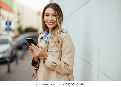 Portrait of a young woman using her phone on a downtown street in urban area. Woman using her phone and looking at the camera. Trendy lady is checking her phone while walking around town. Copy space. - Powered by Shutterstock