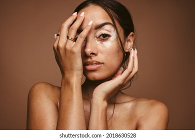 Portrait of young woman with vitiligo on brown background. Close up of woman with skin condition covering her face with hand.