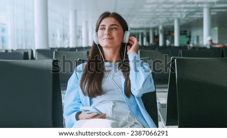 Portrait of young woman waiting airplane or train in waiting room with smartphone in hands. Beautiful woman typing on mobile phone at international airport waiting boarding at airport.