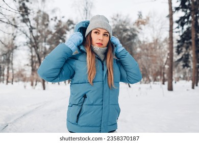 Portrait of young woman walking in snowy winter park wearing blue coat down jacket. Warm clothes for cold weather. - Powered by Shutterstock