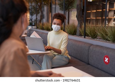 Portrait Of Young Woman Wearing Mask Smiling During Covid Safe Business Meeting In Cafe With Social Distancing, Copy Space