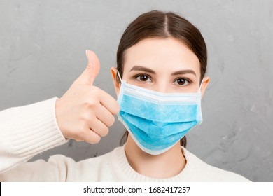 Portrait Of Young Woman Wearing Medical Mask At Gray Cement Background. Person Is Happy Because She Is Finally Healthy. Protect Your Health. Coronavirus Concept.